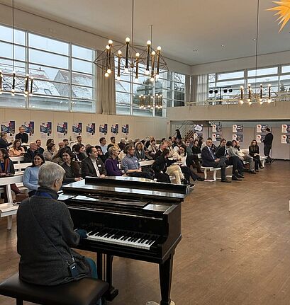 Besucherinnen und Besucher hören Rednerinnen und Rednern sowie einer Pianistin beim Neujahrsempfang im QM-Gebiet Rixdorf zu.