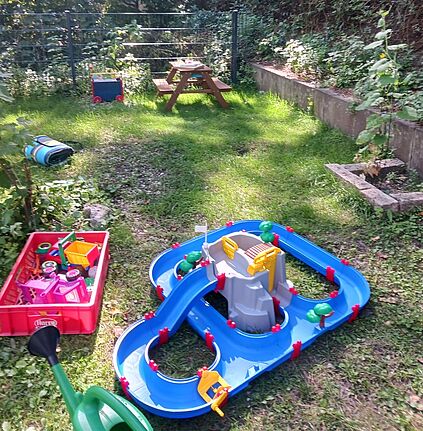 Im Garten des Familienzentrums Lipschitzkids liegen Spielzeug, eine Wasserbahn und eine Holzbank.