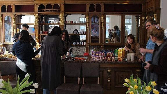 Menschen stehen an einem massiven Holztresen mit Regalen und Spiegeln im neuen Harzer Kiezladen und unterhalten sich.