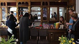 Menschen stehen an einem massiven Holztresen mit Regalen und Spiegeln im neuen Harzer Kiezladen und unterhalten sich.