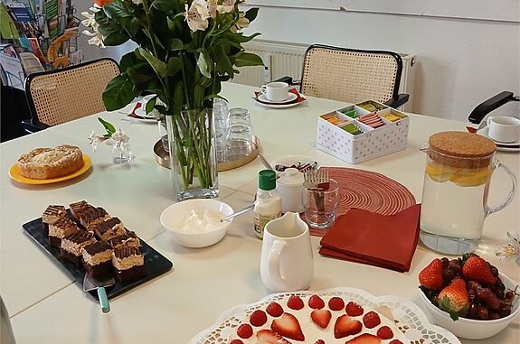 Auf einem Tisch stehen verschiedene Kuchen, Blumen und Tee.