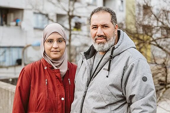 Ahlam Remaid und Ahmad Mahmoud stehen vor einem Hochhaus mit kahlen Bäumen in der High-Deck-Siedlung.