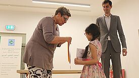 Bildungsstadträtin Karin Korte übergibt eine Medaille an eine Schülerin. Im Hintergrund steht Bezirksbürgermeister Martin Hikel.. 