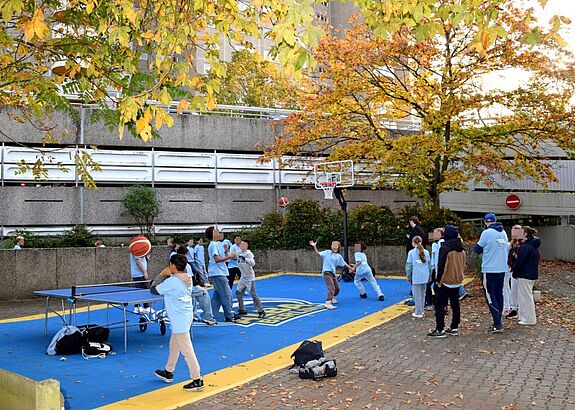Kinder und Jugendliche spielen auf dem Basketballplatz und an der Tischtennisplatte.