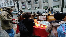 Eine Organisatorin schenkt am Stand vor dem Quartiersbüro zwei Kindern alkoholfreien Punsch aus.