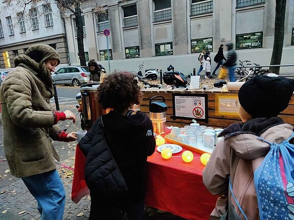 Eine Organisatorin schenkt am Stand vor dem Quartiersbüro zwei Kindern alkoholfreien Punsch aus.