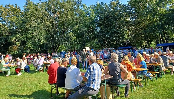 Menschen sitzen bei einem Nachbarschaftsfest im Freien an Biertischen und genießen das Miteinander in der Nahariyastraße.