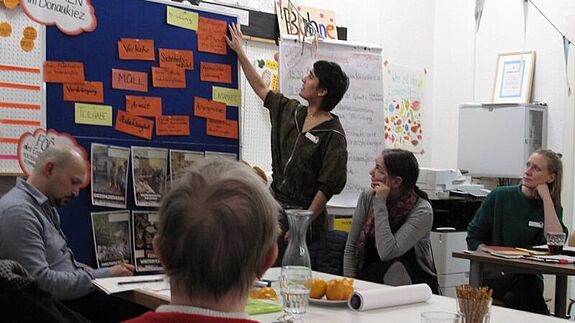 Eine Person zeigt bei einer Quartiersratssitzung im QM-Gebiet Donaustraße-Nord Themen an einer Pinnwand.