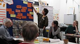 Eine Person zeigt bei einer Quartiersratssitzung im QM-Gebiet Donaustraße-Nord Themen an einer Pinnwand.