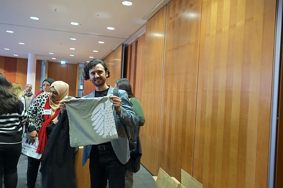 Der Abgeordnete Hakan Demir hält eine Stofftasche mit dem Bundesadler als Andenken nach dem Treffen im Bundestag hoch.