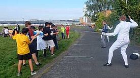 Eine Gruppe Kinder schaut einem Fechter zu