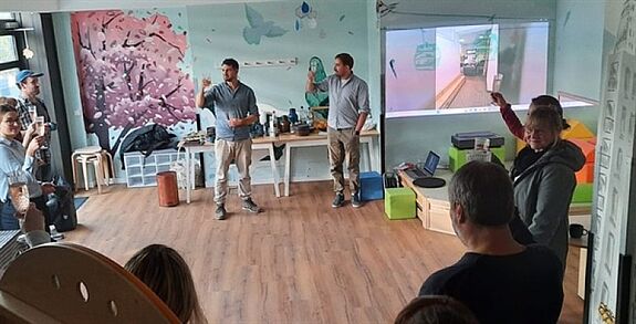 Menschen stehen in einem freundlich gestrichenen Raum mit Wandillustrationen und erheben ihre Gläser.