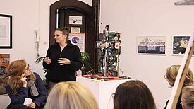 Eine Frau spricht vor mehreren Zuhörerinnen im Müll Museum, im Hintergrund sind Kunstobjekte aus Alltagsgegenständen zu sehen.