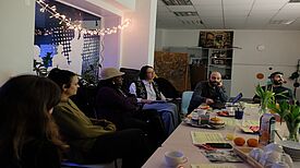 Eine Gruppe von Personen sitzt in gemütlicher Runde um einen gedeckten Tisch.