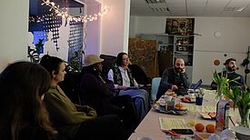 Eine Gruppe von Personen sitzt in gemütlicher Runde um einen gedeckten Tisch.