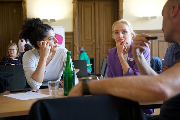 Drei Personen sitzen an einem Tisch und diskutieren engagiert bei der Bildungswerkstatt im Badstraßenkiez.