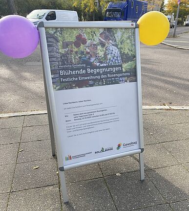 Aufsteller mit Einladung zur festlichen Wiedereröffnung des Rosengartens im QM-Gebiet Titiseestraße, geschmückt mit bunten Luftballons.