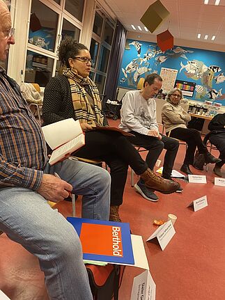 Teilnehmende der Quartiersratssitzung sitzen in einem Stuhlkreis mit Notizbüchern und Namensschildern.