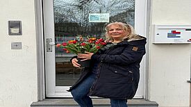 Sidika Özdemir, die ehrenamtlich den Frauentreff organisiert, steht vor einer Tür und hält Blumen.