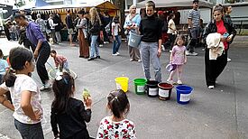 Auf einem Straßenfest werfen Kinder Dinge in fünf verschiedenfarbige, beschriftete Eimer. 