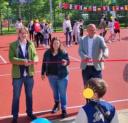 Vertretende aus Politik und Verwaltung durchschneiden gemeinsam ein rotes Band zur Eröffnung der neuen Sportanlagen der KJFE Lessinghöhe.