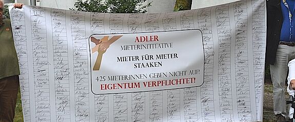 Ein Plakat zeigt viele gesammelte Unterschriften der „Adler-Mieterinitiative“. 