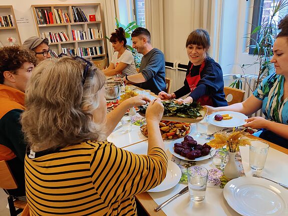 Verschiedene Personen am Tisch teilen das gemeinsam gekochte Essen und jeder tut sich von allem auf.