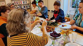 Verschiedene Personen am Tisch teilen das gemeinsam gekochte Essen und jeder tut sich von allem auf.