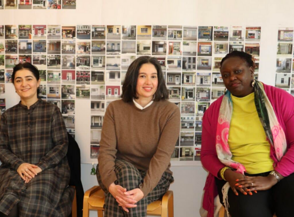 Drei Frauen sitzen während eines Workshops auf einem Hocker und lächeln.