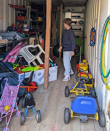 Ein Junge steht im Spielecontainer am Klara-Franke-Spielplatz, umgeben von Spielgeräten und Spielsachen.