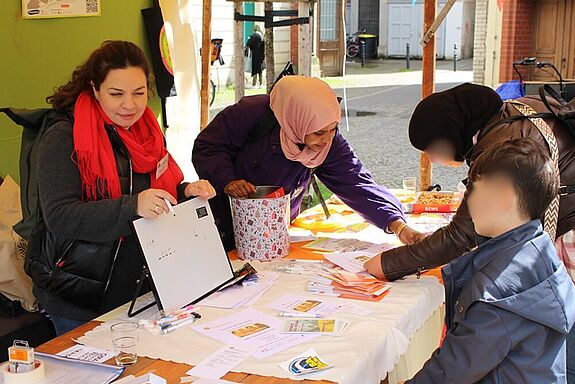 Zwei Personen informieren sich an einem Stand, hinter dem zwei Frauen stehen.