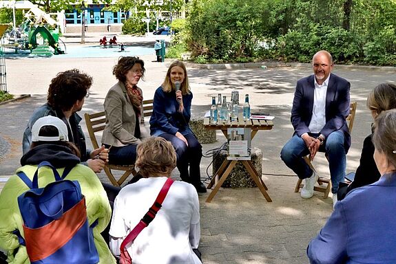 Staatssekretär Stephan Machulik, Bezirksstadträtin Korinna Stephan und Quartiersmanagerin Teresa Rodenfels sitzen an einem Tisch vor einem Publikum.