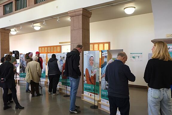 Menschen betrachten Porträt-Aufsteller in einem hellen Foyer mit Säulen.