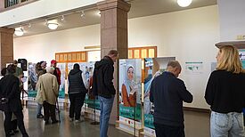 Menschen betrachten Porträt-Aufsteller in einem hellen Foyer mit Säulen.