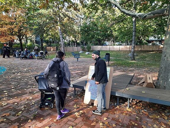 Zwei Personen unterhalten sich im Quartierspark beim Kiezplausch, umgeben von herbstlichen Blättern und weiteren Teilnehmenden im Hintergrund.