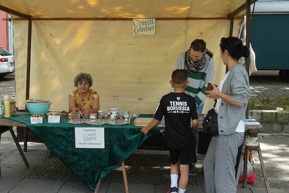 Am Infostand vom Projektträger „Yesil Çember“  informieren sich auf einem Straßenfest ein Kind und eine Frau.