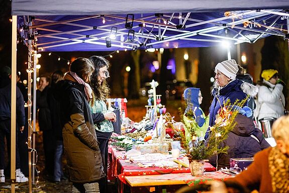 Zwei Personen stehen an einem Stand bei der Tannenbaumaktion im QM-Gebiet Letteplatz und reden mit einer Frau, die hinter dem Stand steht. 