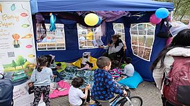 Kinder sitzen auf bunten Kissen in einem Zelt und hören einer der Autorin Romy Mögel zu, die aus einem Buch vorliest.