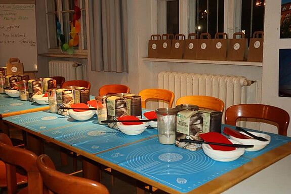 Ein gedeckter Tisch mit Holzstühlen. Auf dem Tisch befinden sich Back-Utensilien und ein Sauerteigstarter.  