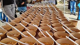 Becher mit der traditionellen Aschura-Süßspeise stehen in Reihen auf einem Tisch unter einem blauen Zelt