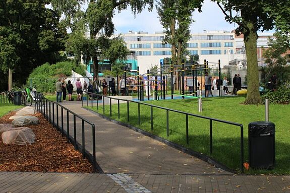 Menschen unterschiedlichen Alters nutzen Calisthenics-Geräte und Aufenthaltsflächen auf dem neuen barrierefrei erreichbaren Spielplatz in der Scheringstraße.