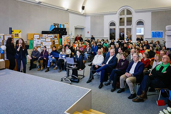 Eine große Gruppe Menschen sitzt beim Neujahresempfang in der Aula der Reginhard-Grundschule vor einer Bühne. 