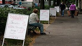 Auftseller mit Fragen, aufgereiht an der Auguste-Viktoria-Allee. Dazwischen Passanten.