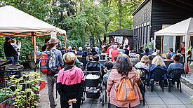 Publikum sitzt im Freien vor einer kleinen Bühne und lauscht einem Musikauftritt beim Kulturfestival „Salon K“ im Lettekiez.