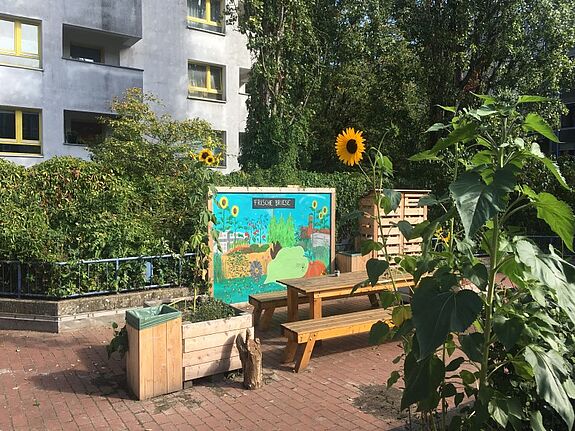 Blumen und Pflanzen blühen rund um eine Tafel und einen großen Tisch im Gemeinschaftsgarten „Frische Briese“. 