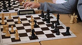 Menschen spielen Schach mit einer Uhr auf dem Tisch.