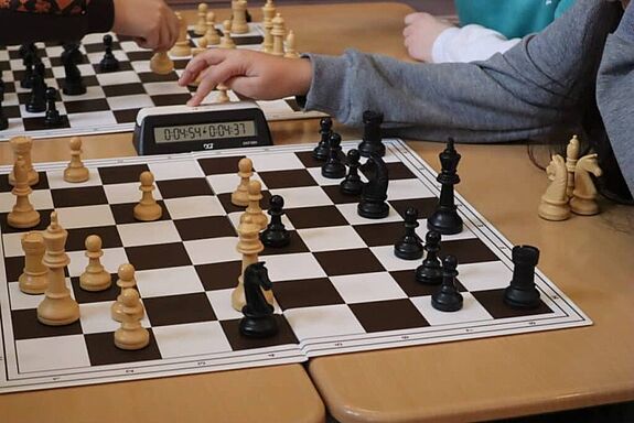 Menschen spielen Schach mit einer Uhr auf dem Tisch.