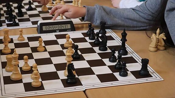 Menschen spielen Schach mit einer Uhr auf dem Tisch.