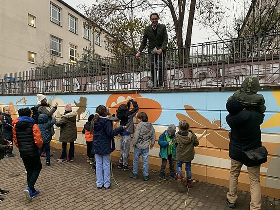 Schulleiter Axel Gotthardt weiht sichtlich erfreut die neue Wandbemalung ein. (Bild: QM Mehringplatz)