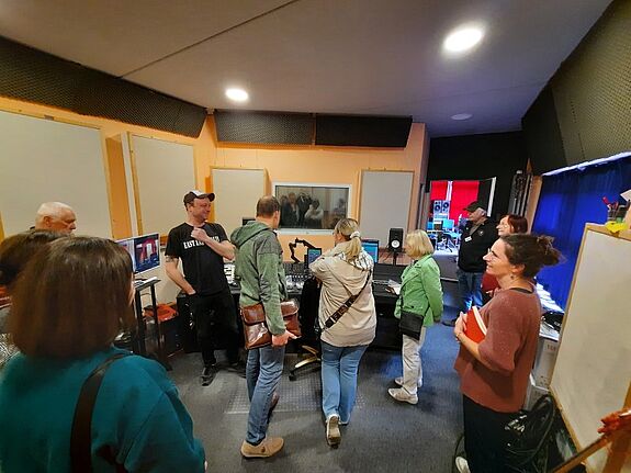 Eine Gruppe von Menschen sitzt im Tonstudio der Jugendfreizeiteinrichtung und hört zu, während der Studiobetreuer die Technik erklärt.